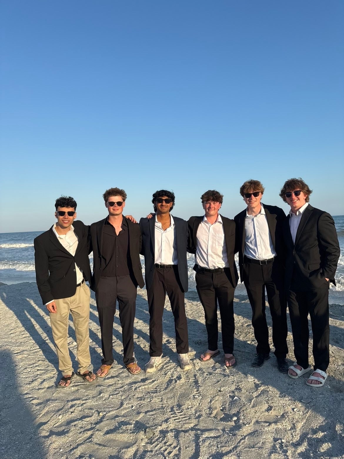 Seven brothers in suits standing on the beach in evening light