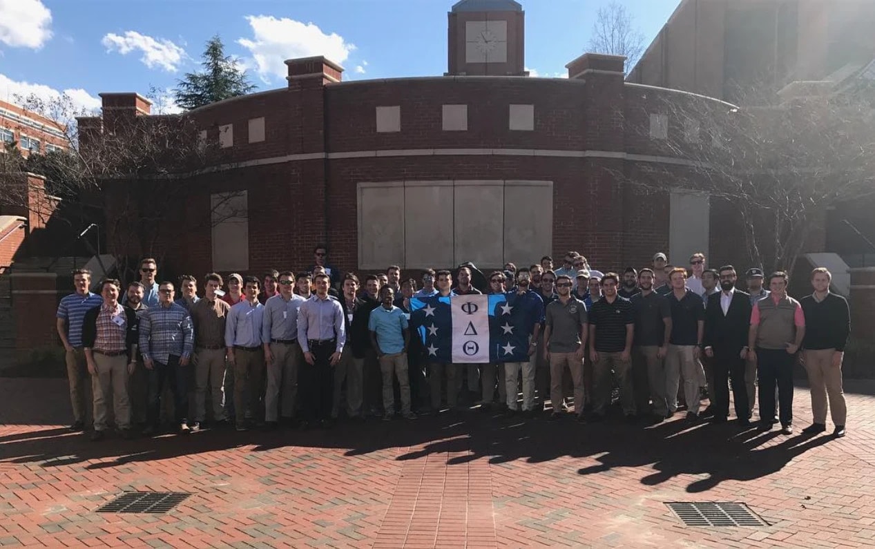 Dozens of NC Epsilon brothers gathered around the Phi Delta Theta flag in a sunny brick courtyard